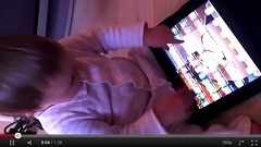 Záběr z videa dítěte s tabletem a časopisy. Celé video můžete vidět níže.